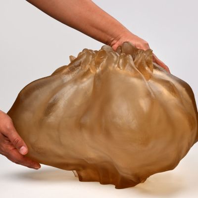 Nana Seydani, Skiftning är en del av kollektion som heter Begränsade Rymder utforskar skärningspunkten mellan hantverk och algoritmisk design genom glasgjutning. Inspirerad av marint liv och Viola Cordovas filosofi om “bounded space”, börjar varje verk som digital kod – en simulering av organiska tillväxtmönster – och får sedan fysisk form genom en taktil, tidskrävande glasgjutning. Verket speglar de gränsrum som formar och förbinder oss: mellan land och vatten, det digitala och det fysiska, det kända och det okända.  Skulpturen blir ett minneskärl – som väcker både igenkänning och främmandeskap – och bjuder in betraktaren att reflektera över sin relation till natur, teknologi och de flytande gränserna däremellan.  Temat Nature Bridge återspeglas i själva metodiken: ett möte mellan det virtuella och det materiella, det mänskliga och det maskinella, där glaset – i egenskap av både naturmaterial  och konstnärligt medium – blir en bro mellan dessa världar. Verket synliggör det ofta osynliga samspelet mellan det vi bygger och det som redan existerar i naturen, mellan minne och transformation, mellan land och hav.  I dialog med platsen – Malmgårdens trädgård, ett historiskt odlingslandskap – framstår skulpturen som ett slags fruset minne av liv under ytan. Den bjuder in till reflektion kring hur vi förhåller oss till naturens former och gränser i en tid av teknologisk acceleration.  ö